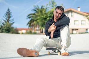 Casual skater smiling at the camera while sitting on their board in the skate park photo