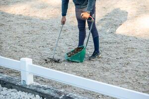 Unrecognizable man cleaning horse manure with rake and scoop at equestrian center photo