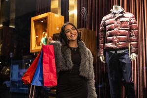 Low-angle shot of smiling young latina shopping through city stores at night photo