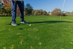 unrecognizable elderly golfer hitting the ball with the putter towards the hole on the green photo