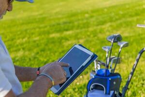 Close-up of senior golfer using tablet on golf course next to golf bag photo