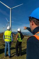 Three multiethnic Engineers observing wind turbines in operation on a hilltop photo