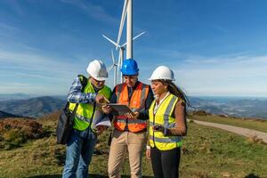 Three multiethnic Engineers using digital tablet analyzing wind turbines in countryside photo
