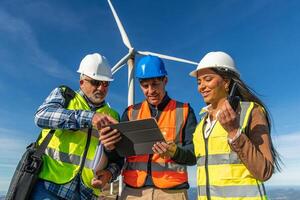 Three multiethnic Engineers using digital tablet, inspecting wind turbine for green energy photo