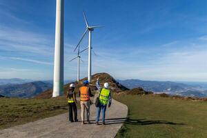 multiethnic Engineers walking and discussing next to wind turbines on mountain top photo