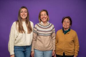 Three generations of women smiling and posing together on purple background photo