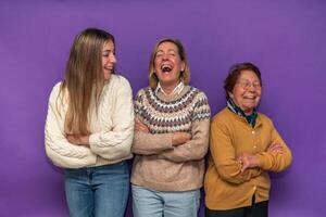 Three generations of women laughing with arms crossed on purple background photo