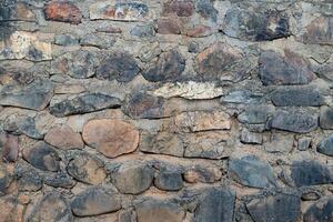 Rough stone wall made of various sized and colored rocks. Creating a textured and uneven surface. photo