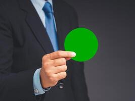 Close-up of hand businessman in a suit holding a blank green circle paper while standing on a gray background photo