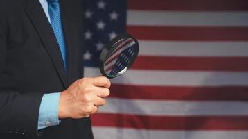 Midsection of a businessman in a suit holding a magnifying glass while standing on the American flag background photo