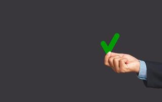 Close-up of hand businessman holding a green check mark symbol at election while standing on a gray background photo