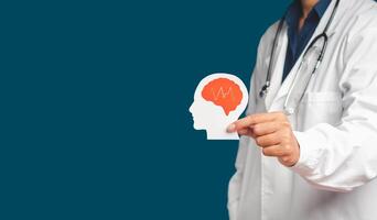 Doctor in uniform holding a white head with a red brain symbol while standing on a blue background photo