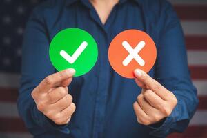 Hands holding red and green papers with a checkmark and cross while standing on the American flag background photo