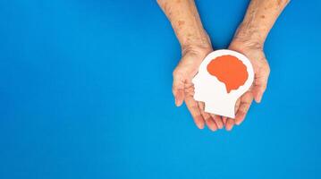 Top view of head with a brain made from paper on the palm senior woman over a blue background photo