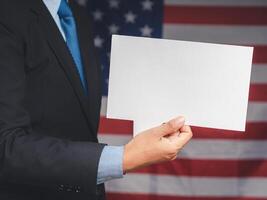 Close-up of a hand businessman holding a blank white speech bubble while standing on the American flag background photo