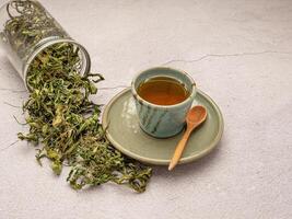 Dry cannabis leaf tea outside a box and marijuana tea cup on a table photo