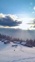 A photographer stands in deep snow, using a tripod to capture the stunning winter landscape. The sun sets behind clouded mountains. Vertical footage video