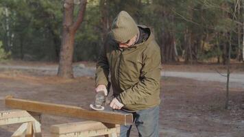 An experienced man uses a power tool to process a metal beam while standing in a serene forest. The sun shines through the trees, enhancing the tranquil atmosphere. video