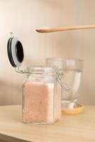 A jar of Himalayan salt sits on a table, with a wooden spoon scooping some. photo