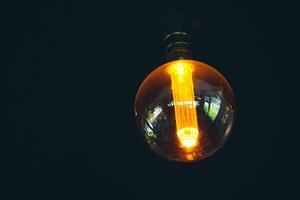 Vintage Edison Light Bulb Glowing in Dark Room with Warm Ambient Light and Reflections on Glass Surface photo