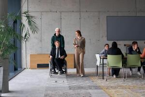 A diverse team of business colleagues, including a director in a wheelchair, engages in a collaborative discussion as they move together through a modern office space photo