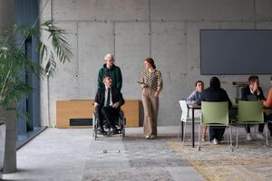A diverse team of business colleagues, including a director in a wheelchair, engages in a collaborative discussion as they move together through a modern office space photo
