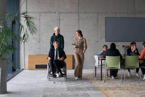 A diverse team of business colleagues, including a director in a wheelchair, engages in a collaborative discussion as they move together through a modern office space photo