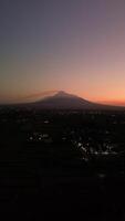 4k aerial footage of Mount Merapi from a distance when it was still dark before sunrise. The panorama towards the morning of the active volcano from a distance is still a silhouette with a thin light video