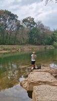 The activity of fishing alone on the edge of a calm and quiet river. 4k footage of an angler fishing waiting for his bait to be eaten by fish on the edge of a clear river full of rocks. video