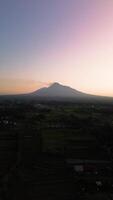 4k portrait of an active volcano in detail with a green forest in front. Portrait footage from an aerial drone shows a panorama of Mount Merapi from a distance with beautiful views in the morning video