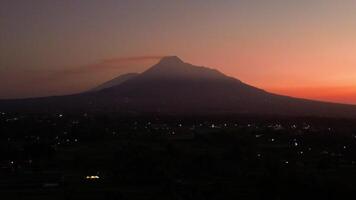 4k aerial footage of Mount Merapi from a distance when it was still dark before sunrise. The panorama towards the morning of the active volcano from a distance is still a silhouette with a thin light video