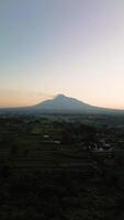 4k portrait of an active volcano in detail with a green forest in front. Portrait footage from an aerial drone shows a panorama of Mount Merapi from a distance with beautiful views in the morning video