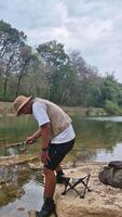 The activity of fishing alone on the edge of a calm and quiet river. 4k footage of an angler fishing waiting for his bait to be eaten by fish on the edge of a clear river full of rocks. video