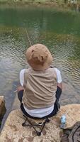 The activity of fishing alone on the edge of a calm and quiet river. 4k footage of an angler fishing waiting for his bait to be eaten by fish on the edge of a clear river full of rocks. video