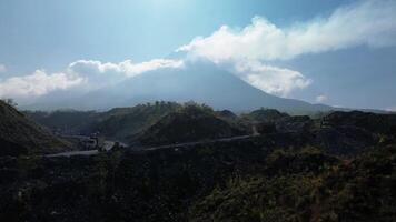 Panorama of a volcano with a barren area in the foreground with a winding road surrounded by piles of rocks and sand left over from the fall of volcanic material during an eruption video