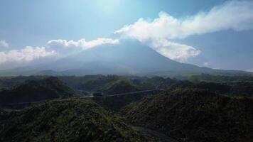 Panorama of a volcano with a barren area in the foreground with a winding road surrounded by piles of rocks and sand left over from the fall of volcanic material during an eruption video