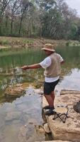 The activity of fishing alone on the edge of a calm and quiet river. 4k footage of an angler fishing waiting for his bait to be eaten by fish on the edge of a clear river full of rocks. video