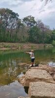 The activity of fishing alone on the edge of a calm and quiet river. 4k footage of an angler fishing waiting for his bait to be eaten by fish on the edge of a clear river full of rocks. video