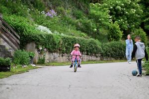 A group of children, including a boy and girl playing with a ball and their young friend riding a bike, enjoying a fun filled day in a natural outdoor setting photo