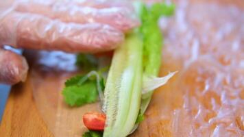 Side view of a sushi chef hands leveling triangle Japanese roll in rice paper, close up, kitchen workplace with fresh vegetables and herbs. video