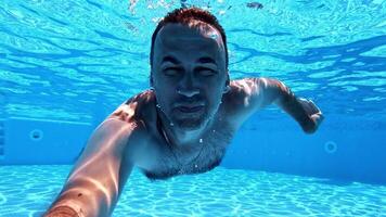 Man swimming underwater. Healthy man diving in the swimming pool and looking at camera. Happy male showing ok sign inside the pool. video