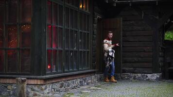Man walks out a wooden house with big blanket in hands. Autumn evening outside. video
