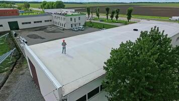 Worker in safety helmet on rooftop. Engineer standing on a flat roof of a big builduing in summer. Development of solar farm from roof. Aerial view. video