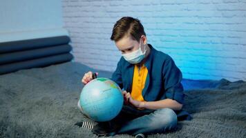 Child in Self isolation looking at globe learning about Covid-19. Boy in a medical mask with curious face thinking about the planet during covid lock down, quarantine and social distancing concept video