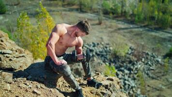 Handsome sportsman with a dumbbell outdoors. Muscular athlete pumping his arm biceps on the rocky background in summer day. video