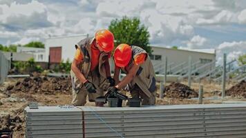 Solar plant construction. Two workers in orange helmets prepare instruments for building solar panels. Engineers installing metal basis for future solar power plant. video