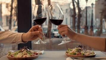 Two diners raise their glasses of red wine in a toast while enjoying fresh salads at a charming restaurant. The warm atmosphere enhances their intimate moment during dinner. video