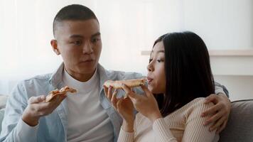 A young couple sits comfortably together, sharing slices of pizza and engaging in a light-hearted conversation. The atmosphere is relaxed and cozy, highlighting their connection. video