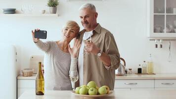 A couple smiles as they take a selfie together in a bright kitchen, surrounded by a bottle of wine and a bowl of fresh green apples, creating a warm and inviting atmosphere. video