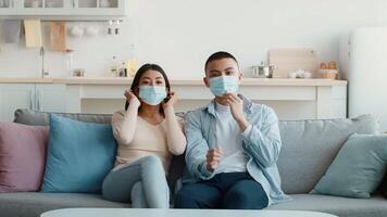 A young couple sits closely together on a comfortable sofa in a well-lit living room, both wearing masks. They appear calm and content, navigating life during the pandemic. video